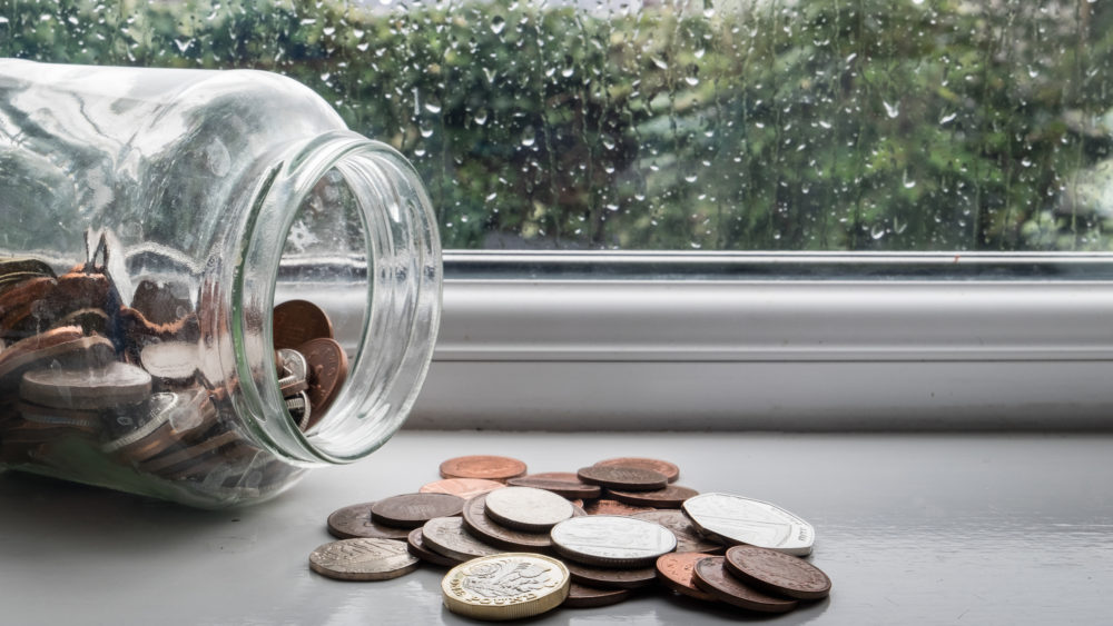 A jar of money tipped over with a rainy day in the background