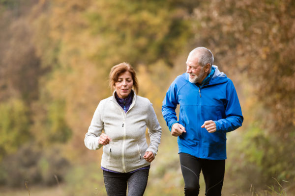An older couple jogging through a forest in autumn