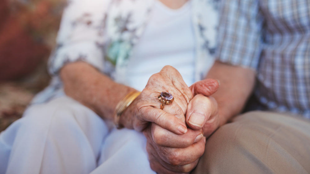 A close up of an elderly couple holding hands.
