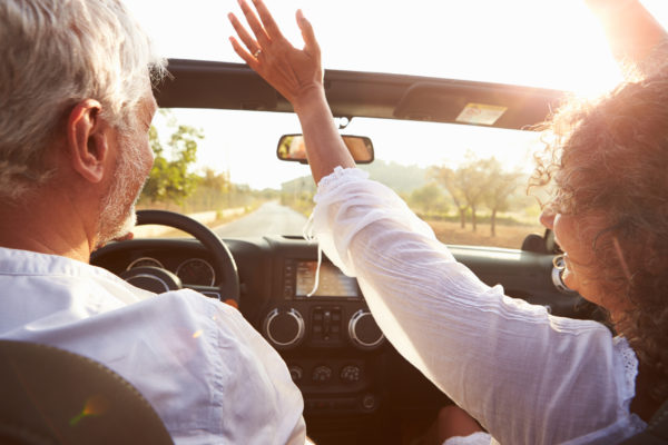 An older couple driving in an open-top car.