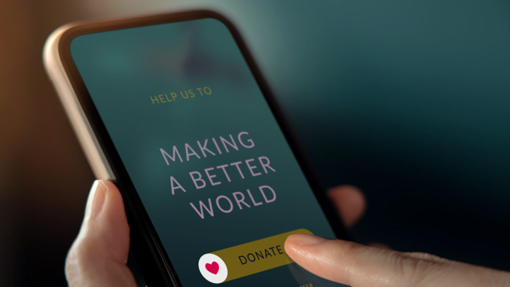 Someone holding a phone and pressing a “donate” button on the screen.