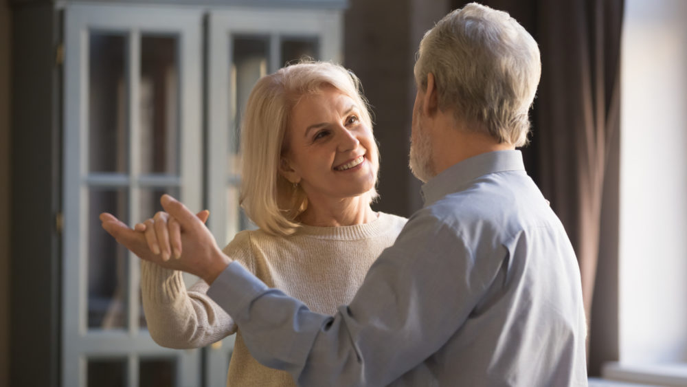 A smiling senior couple dance in their living room