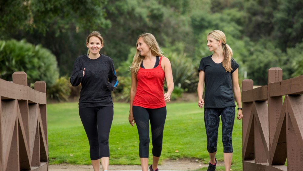 Three women in gym clothes walking over a bridge