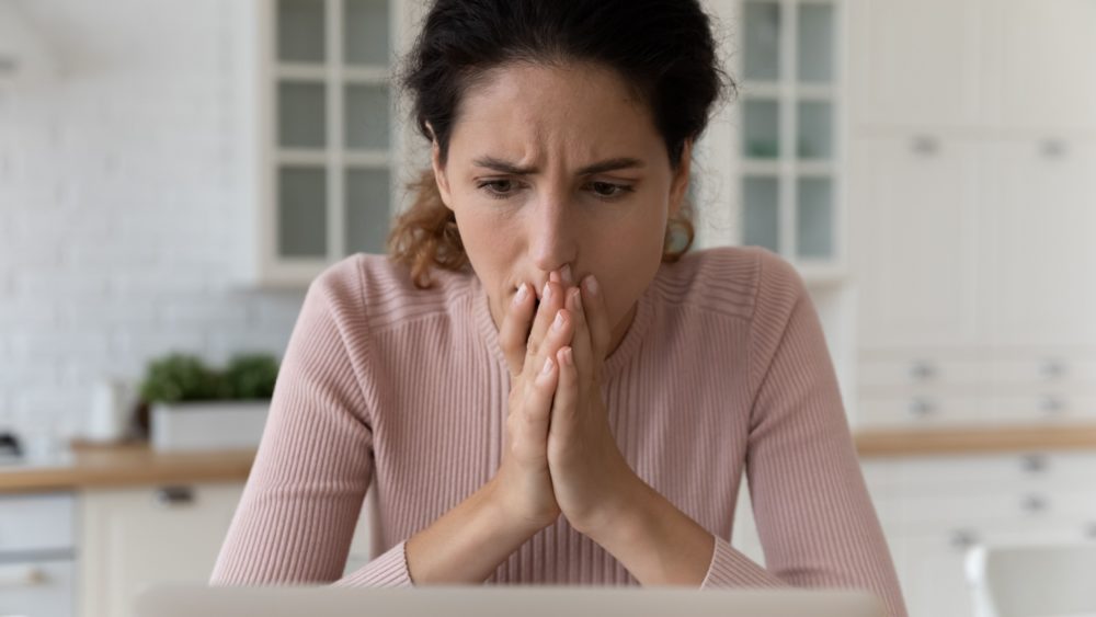 A woman looks at her laptop in shock.