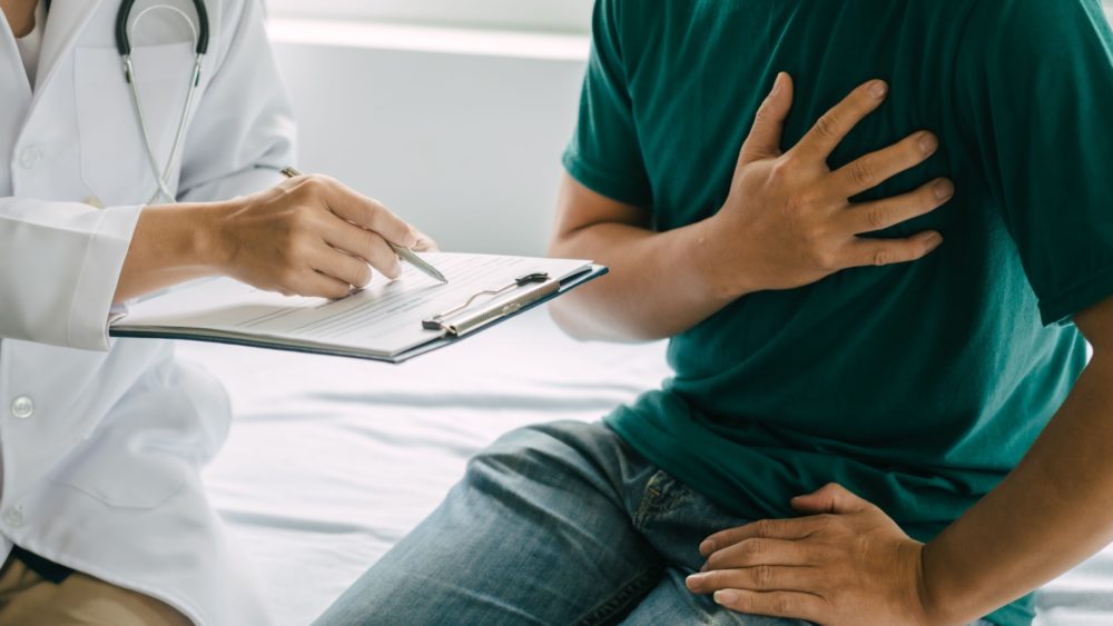 A man clutching his heart while a doctor examines him.