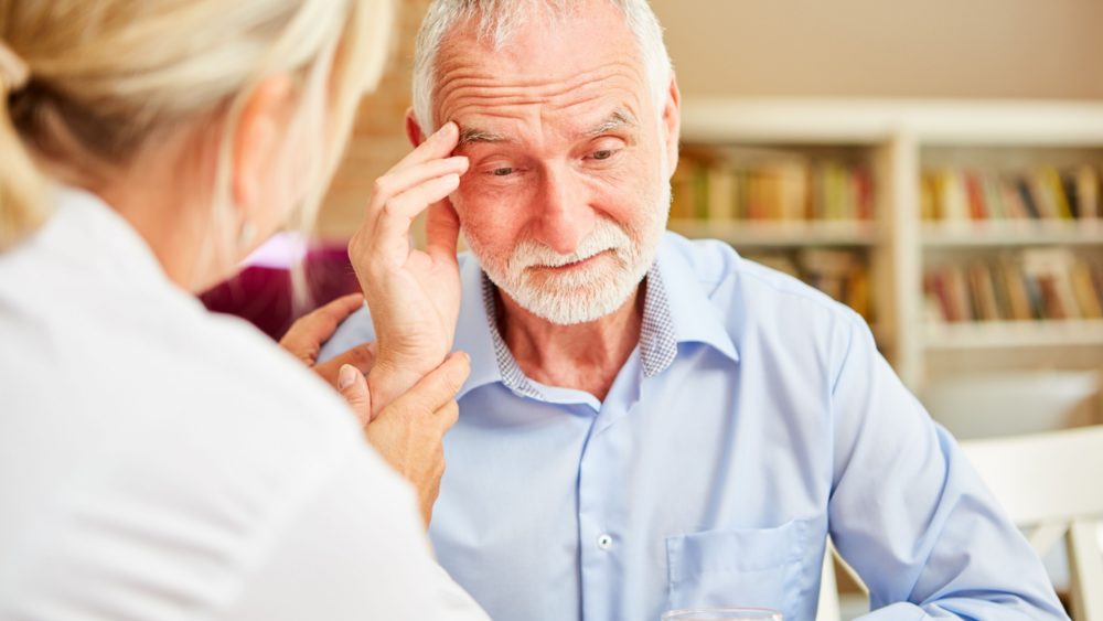 An older man touching his head in confusion while a doctor comforts him.