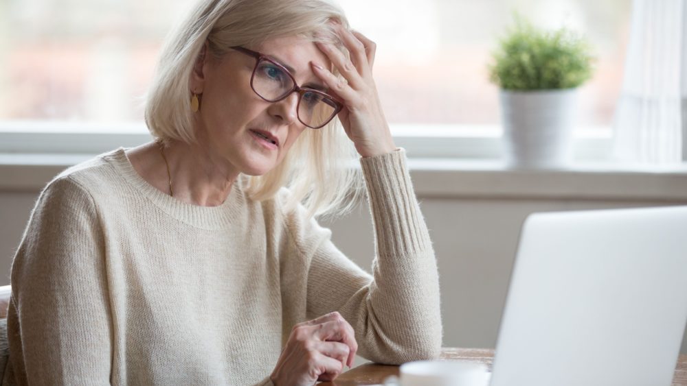 A retired woman looking worried while using a laptop.