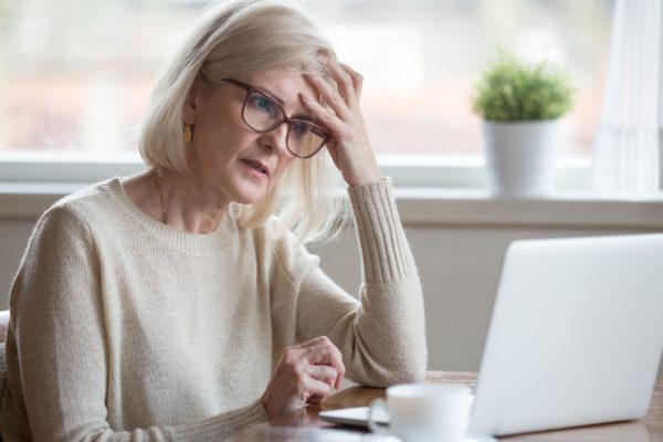 A retired woman looking worried while using a laptop.