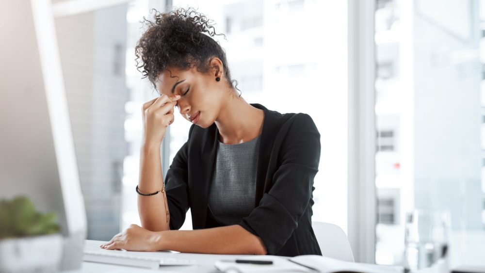 A woman pinching the bridge of her nose in an office.