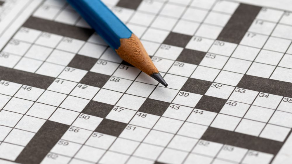 A close-up of an empty crossword puzzle with a pencil lying on top.