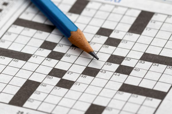 A close-up of an empty crossword puzzle with a pencil lying on top.