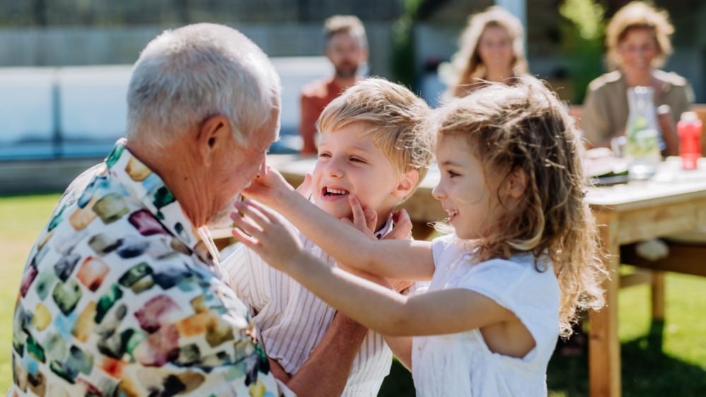 A grandfather playing with his grandchildren outdoors.
